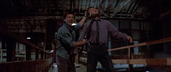 Movie still from “Big Trouble in Little China” (1986), directed by John Carpenter – Two men are holding guns in a room; Medium shot, Low angle