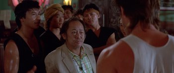 Movie still from “Big Trouble in Little China” (1986), directed by John Carpenter – A group of men standing in a room; Medium shot, Over the shoulder angle