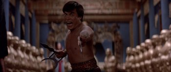 Movie still from “Big Trouble in Little China” (1986), directed by John Carpenter – A man holding a knife in his hand and smiling for the camera; Medium shot, Low angle