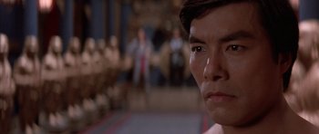 Movie still from “Big Trouble in Little China” (1986), directed by John Carpenter – A man's face in front of a group of people; Close Up shot, Over the shoulder angle