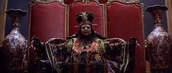 Movie still from “Big Trouble in Little China” (1986), directed by John Carpenter – A man with a beard wearing a crown sitting in a chair; Wide shot, High angle