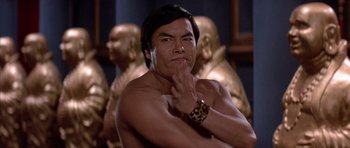 Movie still from “Big Trouble in Little China” (1986), directed by John Carpenter – A man with his arms crossed in front of some statues; Close Up shot, Low angle