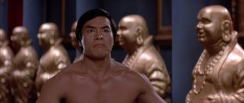 Movie still from “Big Trouble in Little China” (1986), directed by John Carpenter – A shirtless man standing in front of statues; Close Up shot, Low angle
