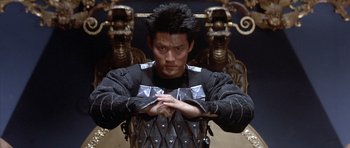 Movie still from “Big Trouble in Little China” (1986), directed by John Carpenter – A man in a black and silver outfit standing in front of an ornate wall; Medium shot, Low angle