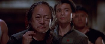 Movie still from “Big Trouble in Little China” (1986), directed by John Carpenter – Two asian men standing next to each other in a room; Close Up shot, Over the shoulder angle