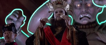 Movie still from “Big Trouble in Little China” (1986), directed by John Carpenter – A man with a beard and a crown is holding a chopstick; Close Up shot, Low angle