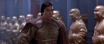 Movie still from “Big Trouble in Little China” (1986), directed by John Carpenter – A man in a brown and gold outfit standing in front of statues; Medium shot, Low angle