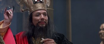 Movie still from “Big Trouble in Little China” (1986), directed by John Carpenter – A man with a long beard wearing a crown and holding a cigarette; Close Up shot, Over the shoulder angle