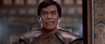 Movie still from “Big Trouble in Little China” (1986), directed by John Carpenter – An asian man in a brown and silver outfit; Close Up shot, Low angle