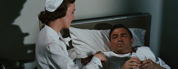 Movie still from “Bigger Than Life” (1956), directed by Nicholas Ray – A nurse is helping a man in a hospital bed; Medium shot, Over the shoulder angle