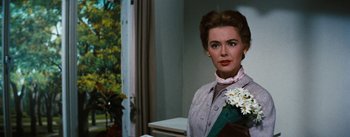 Movie still from “Bigger Than Life” (1956), directed by Nicholas Ray – A woman holding a bouquet of flowers while standing next to a window; Close Up shot, Over the shoulder angle