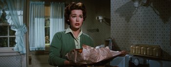 Movie still from “Bigger Than Life” (1956), directed by Nicholas Ray – A woman in a green sweater holding a bag of food; Medium shot, Over the shoulder angle