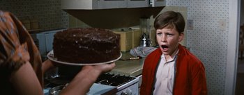 Movie still from “Bigger Than Life” (1956), directed by Nicholas Ray – A person holding a plate with a cake in front of a boy; Close Up shot, High angle
