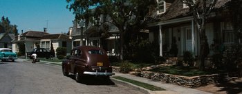 Movie still from “Bigger Than Life” (1956), directed by Nicholas Ray – An old car parked on the side of the street; Wide shot, High angle