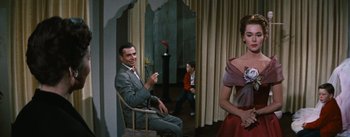 Movie still from “Bigger Than Life” (1956), directed by Nicholas Ray – A man sitting in a chair in front of two women; Medium shot, Over the shoulder angle