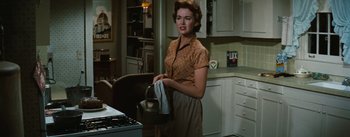 Movie still from “Bigger Than Life” (1956), directed by Nicholas Ray – A woman in a kitchen holding a basket of food; Medium shot, Low angle