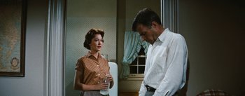 Movie still from “Bigger Than Life” (1956), directed by Nicholas Ray – An older woman standing next to an older man in a room; Medium shot, Low angle