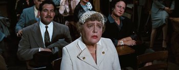 Movie still from “Bigger Than Life” (1956), directed by Nicholas Ray – An older woman wearing a white suit and a hat; Close Up shot, Over the shoulder angle