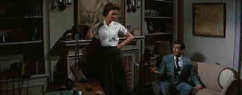 Movie still from “Bigger Than Life” (1956), directed by Nicholas Ray – A woman standing in front of a man in a living room; Medium shot, High angle