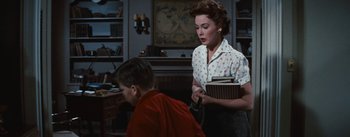 Movie still from “Bigger Than Life” (1956), directed by Nicholas Ray – An older woman holding a book and a young boy sitting on the floor; Medium shot, Low angle