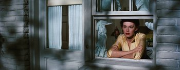 Movie still from “Bigger Than Life” (1956), directed by Nicholas Ray – A woman sitting on a window sill looking out of a window; Medium shot, Over the shoulder angle