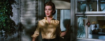 Movie still from “Bigger Than Life” (1956), directed by Nicholas Ray – A woman in a yellow shirt standing in front of a door; Medium shot, Low angle