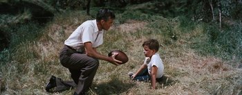 Movie still from “Bigger Than Life” (1956), directed by Nicholas Ray – A man and a boy are playing football in a field; Medium shot, High angle