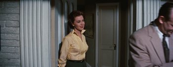 Movie still from “Bigger Than Life” (1956), directed by Nicholas Ray – A woman in a yellow shirt standing next to a doorway; Medium shot, Low angle