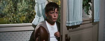Movie still from “Bigger Than Life” (1956), directed by Nicholas Ray – A young boy holding a football in his hand; Medium shot, High angle