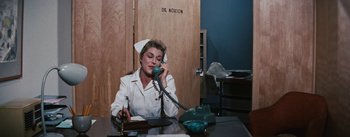 Movie still from “Bigger Than Life” (1956), directed by Nicholas Ray – A woman sitting at a table talking on a phone; Medium shot, Low angle