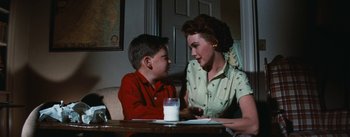 Movie still from “Bigger Than Life” (1956), directed by Nicholas Ray – A woman and a boy sitting at a table; Medium shot, Over the shoulder angle