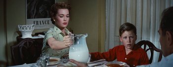 Movie still from “Bigger Than Life” (1956), directed by Nicholas Ray – A woman and a child at a table with a pitcher of milk in front of them; Medium shot, Over the shoulder angle