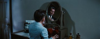 Movie still from “Bigger Than Life” (1956), directed by Nicholas Ray – A man looking in a mirror while holding a cell phone; Medium shot, Over the shoulder angle
