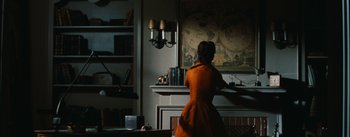 Movie still from “Bigger Than Life” (1956), directed by Nicholas Ray – A woman in an orange dress standing in front of a fire place; Wide shot, Over the shoulder angle