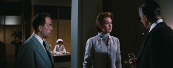 Movie still from “Bigger Than Life” (1956), directed by Nicholas Ray – A woman standing in front of a desk in a room; Medium shot, Low angle
