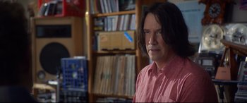 Movie still from “Bill & Ted Face the Music” (2020), directed by Dean Parisot – A man with long hair is standing in front of a book shelf; Close Up shot, Over the shoulder angle