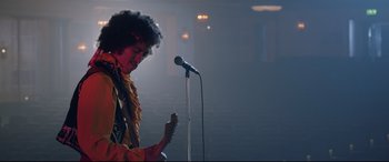 Movie still from “Bill & Ted Face the Music” (2020), directed by Dean Parisot – A man playing a guitar on a stage with a microphone in front of him; Medium shot, Low angle