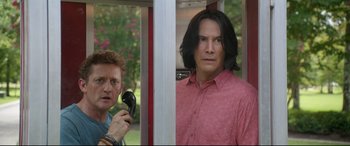 Movie still from “Bill & Ted Face the Music” (2020), directed by Dean Parisot – A man with long black hair and a pink shirt is holding a hair dryer; Medium shot, Low angle