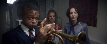 Movie still from “Bill & Ted Face the Music” (2020), directed by Dean Parisot – A man playing a trumpet while two women look on; Medium shot, Low angle