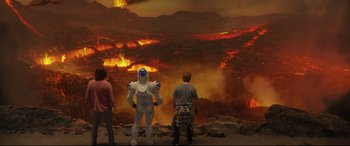 Three people are standing in front of an erupting volcano