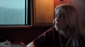 Movie still from “Billie Eilish: The World's a Little Blurry” (2021), directed by R.J. Cutler – A woman sitting in front of a window looking off into the distance; Close Up shot, High angle