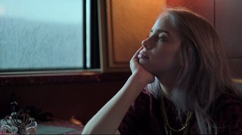 Movie still from “Billie Eilish: The World's a Little Blurry” (2021), directed by R.J. Cutler – A woman sitting at a table with her hand under her chin; Close Up shot, Low angle