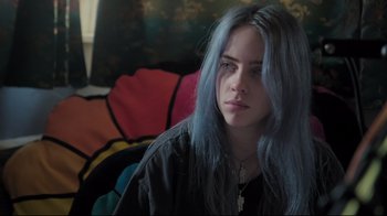 Movie still from “Billie Eilish: The World's a Little Blurry” (2021), directed by R.J. Cutler – A woman with blue hair sitting on a couch; Close Up shot, High angle