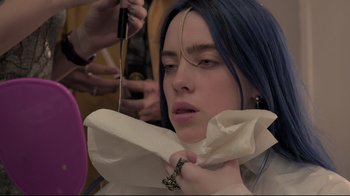 Movie still from “Billie Eilish: The World's a Little Blurry” (2021), directed by R.J. Cutler – A woman with long blue hair is getting her hair cut; Close Up shot, Over the shoulder angle