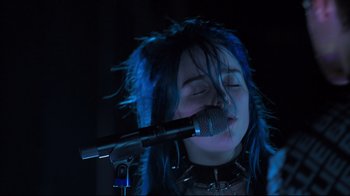 Movie still from “Billie Eilish: The World's a Little Blurry” (2021), directed by R.J. Cutler – A woman with blue hair is singing into a microphone; Close Up shot, Low angle