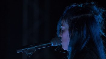 Movie still from “Billie Eilish: The World's a Little Blurry” (2021), directed by R.J. Cutler – A woman with blue hair is singing into a microphone; Close Up shot, Low angle