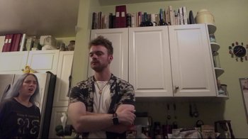 Movie still from “Billie Eilish: The World's a Little Blurry” (2021), directed by R.J. Cutler – A man standing in front of a kitchen counter with his arms crossed; Medium shot, Low angle