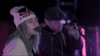 Movie still from “Billie Eilish: The World's a Little Blurry” (2021), directed by R.J. Cutler – A woman in a hat is singing into a microphone; Close Up shot, Over the shoulder angle