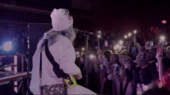 Movie still from “Billie Eilish: The World's a Little Blurry” (2021), directed by R.J. Cutler – A person on a stage with a microphone; Wide shot, High angle