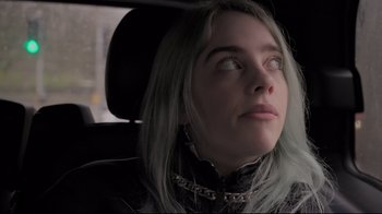 Movie still from “Billie Eilish: The World's a Little Blurry” (2021), directed by R.J. Cutler – A woman sitting in the back seat of a car; Close Up shot, Over the shoulder angle